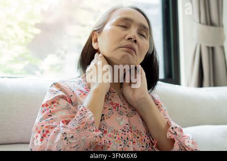 Portrait d'une femme asiatique mûre inclinant la tête en arrière et touchant son cou, souffrant de douleurs cervicales chroniques ou d'un cou raide. Banque D'Images