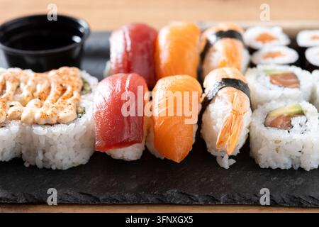 Close-up d'un plateau d'assortiment de sushi comprenant des nigiris au saumon, au thon et aux crevettes avec des rouleaux maki, servis sur une planche d'ardoise sombre. Concept de nourriture japonaise. Banque D'Images