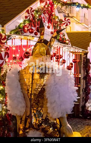 Bialystok, Pologne – 4 décembre 2025 : Artiste vêtu d’un costume de lapin miroir doré se tient devant des étals de marché de Noël décorés avec des ornements de bonbons Banque D'Images