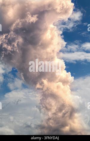 Un nuage cumulus imposant s'élève contre un ciel bleu vif, illuminé par les tons chauds du coucher de soleil. Banque D'Images
