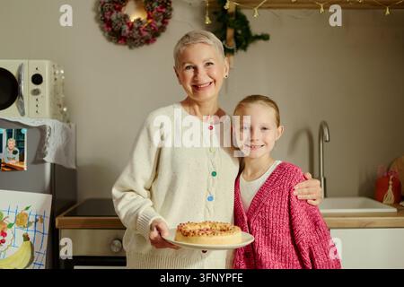 Portrait d'une femme âgée et d'une fille tenant un gâteau dans la cuisine Banque D'Images
