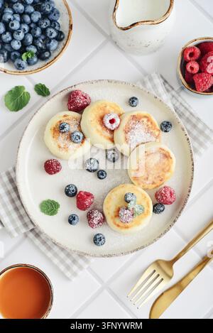 Crêpes au fromage frais avec des myrtilles fraîches, des framboises et de la menthe sur une assiette, servies avec une tasse de thé, un couteau, une fourchette et une serviette en tissu à carreaux Banque D'Images