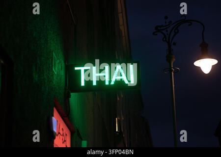 Hongrie, Budapest 2021 09 05 : Gros plan d'un panneau néon LED vert vif d'un restaurant thaïlandais brillant sur un mur de rue sombre la nuit, illuminé par un n Banque D'Images