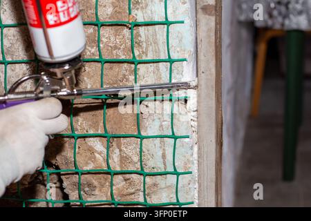 Un gros plan d'une main appliquant de la mousse de polyuréthane expansible avec un pistolet à pulvériser pour sceller un vide de construction. Processus de rénovation résidentielle. Amélioration de l'habitat Banque D'Images