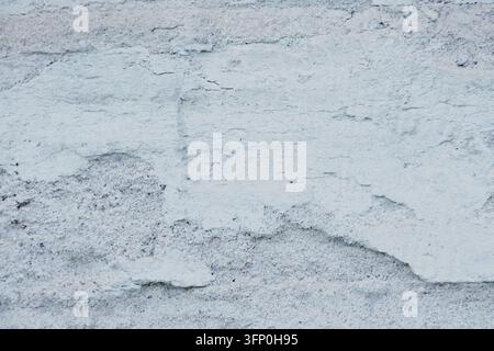 Ancienne surface en ciment grungy avec une couche de plâtre rugueux bleu clair, des fissures et un relief texturé irrégulier. Banque D'Images