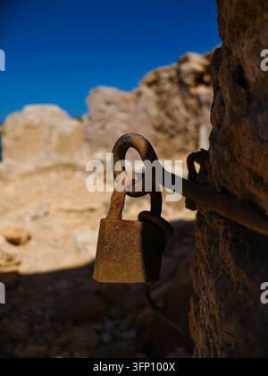 Un gros plan d'un vieux cadenas en métal rouillé et d'une chaîne attachés à un mur de pierre rugueux et usé à Campos, en Espagne. Le ciel bleu profond est visible dans le Banque D'Images