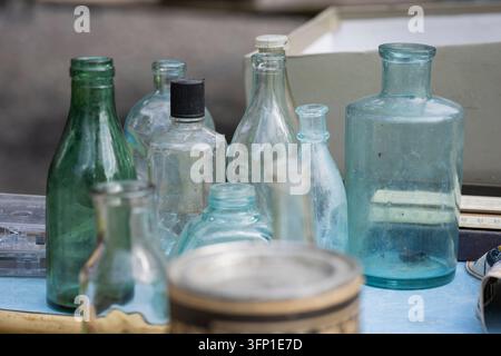 Bouteilles en verre vintage dans des teintes de vert, bleu et transparent disposées sur une table de marché, mettant en valeur des formes variées, des textures de verre vieilles. Banque D'Images
