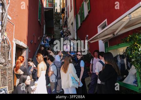 Varenna, Italie - avril, 05, 2026 : Un groupe de personnes se tient et interagit dans une ruelle étroite près d'une crèmerie glacée Banque D'Images