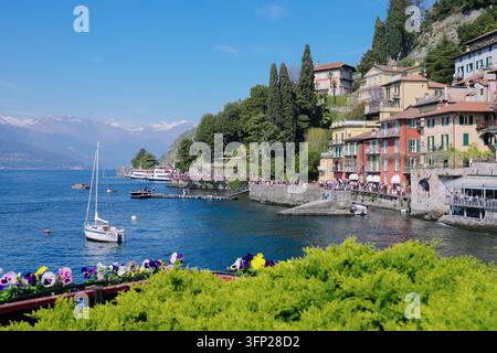 Varenna, Italie - 5 avril 2026 : Voilier sur le lac de Côme près des maisons colorées du village italien avec des terrasses remplies de fleurs Banque D'Images