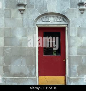 Une porte rouge se trouve sous un panneau semi-circulaire sculpté dans une façade en pierre. Banque D'Images
