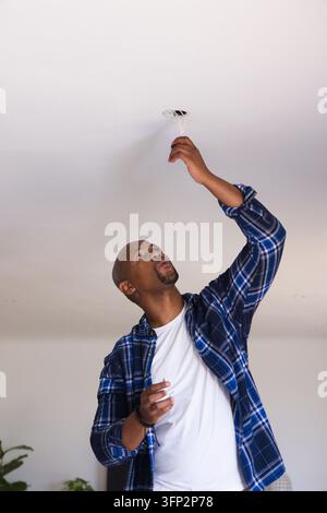Homme adulte debout sous un plafond blanc, portant une chemise à carreaux bleus, atteignant une boîte électrique ouverte Banque D'Images