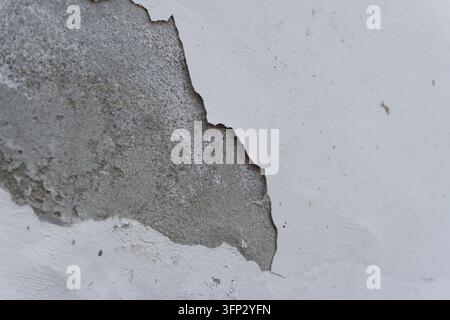 Peinture blanche écaillée sur un mur révélant le plâtre gris en dessous, gros plan d'une surface murale endommagée Banque D'Images