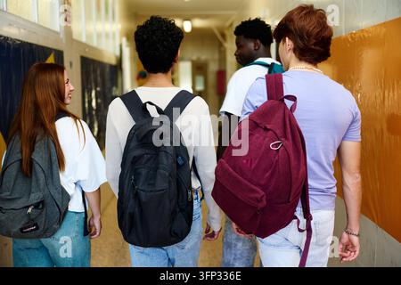 Groupe divers d'élèves du lycée marchant par derrière dans un couloir scolaire vibrant portant des sacs à dos Banque D'Images