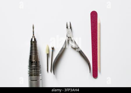 Set de manucure avec une perceuse à ongles électrique, des embouts, des pinces et une lime à ongles sur fond blanc. Outils de soins des ongles et de manucure Banque D'Images