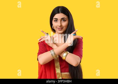 Diversité culturelle et mode traditionnelle, jeune Indienne en sari rouge avec des bijoux posant sur un fond jaune Banque D'Images