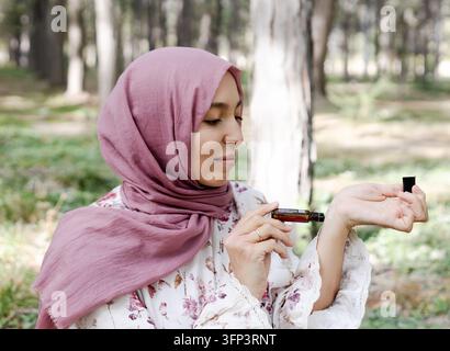 Femme musulmane en hijab appliquant une huile essentielle sur son poignet et tenant une bouteille d'huile essentielle Banque D'Images