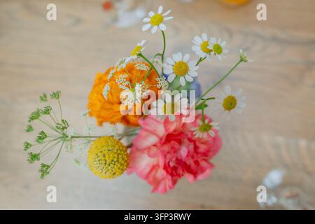Bouquet de fleurs disposé dans un vase, sur une table en bois, avec des marguerites, des soucis, une pivoine rose, une fleur sphérique jaune, vue de dessus Banque D'Images