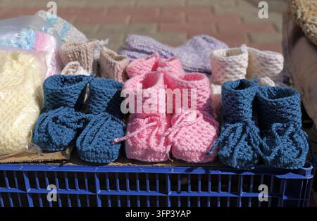 Des chaussons tricotés à la main colorés sont soigneusement disposés sur une caisse en plastique bleue, mettant en valeur l’artisanat local et offrant une douce chaleur pour les nourrissons Banque D'Images