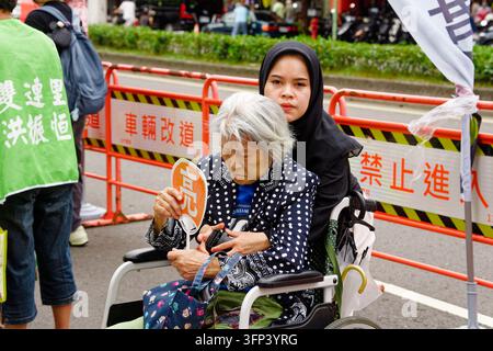 Taipei, Taïwan - 03 oct. 2026 : Une aide-soignante migrante portant un hijab s'occupe d'une femme âgée en fauteuil roulant tenant un éventail à côté des barrières "No Entry". Banque D'Images
