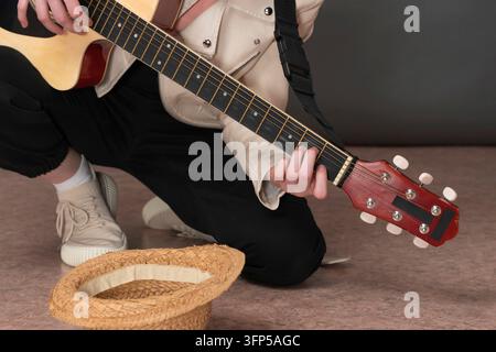 Musicienne de rue guitariste jouant de la guitare acoustique pour de l'argent et devant son chapeau de paille vide pour les dons à la guitare. Femme non identifiable kn Banque D'Images