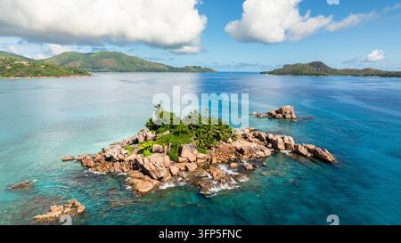 Île rocheuse couverte d'une végétation vibrante, entourée d'eaux turquoise et de collines lointaines. Île Saint-Pierre. Seychelles. Banque D'Images