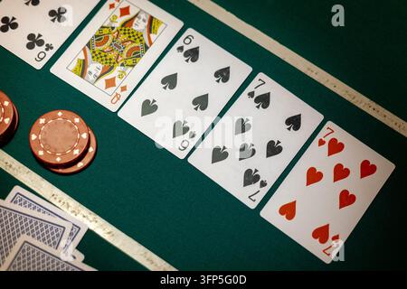 Tapis de poker vert présentant cinq cartes à jouer ouvertes en ligne à côté de jetons de paris ronds rouges. Le plateau affiche le six de trèfle, la dame de carreau, le six de pique. Banque D'Images