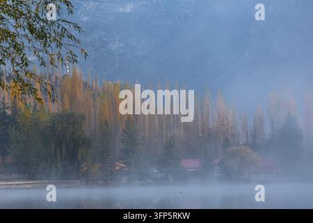 Vue du lac Lower Kachura entouré d'arbres automnaux brumeux et de montagnes à Skardu, Gilgit Baltistan, Pakistan. Banque D'Images