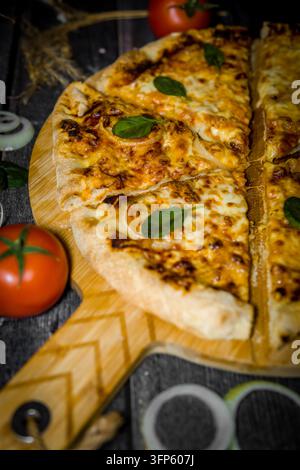 Close up d'une délicieuse pizza fraîchement cuite tranchée sur une planche en bois avec des ingrédients Banque D'Images