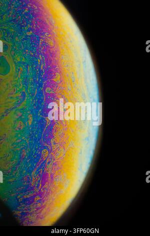 Grossissement macro d'une surface de bulle de savon iridescente montrant des couleurs arc-en-ciel cosmiques vibrantes sur un fond sombre Banque D'Images