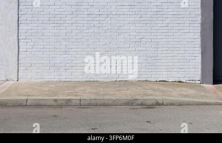 Mur de briques peint en blanc au bord de la route avec trottoir en béton et route devant. Arrière-plan pour espace de copie. Banque D'Images