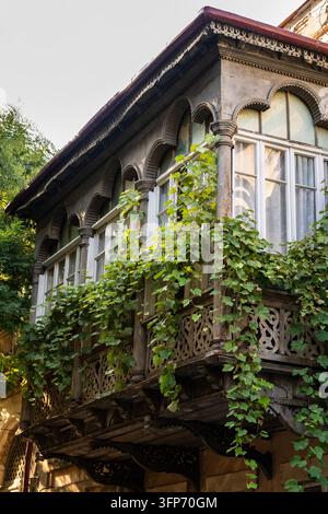 Façade d'immeuble résidentiel historique avec balcon en bois sculpté traditionnel et verdure à Tbilissi. Banque D'Images