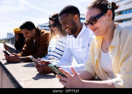 Des amis divers utilisant des smartphones en plein air et profitant de la technologie Banque D'Images