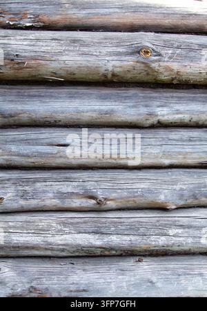 Close-up d'un vieux mur de maison en bois fait de rondins gris horizontaux avec des fissures et des nœuds. Texture de bois naturellement vieilli dans un style rustique. Fragment de Banque D'Images