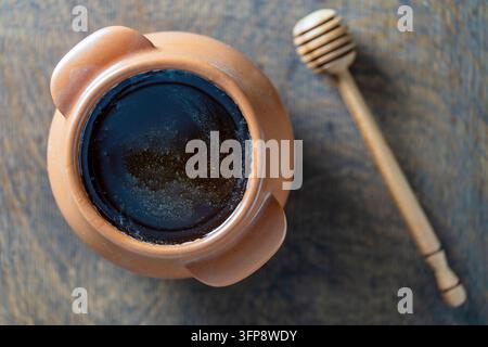 Miel brut dans un pot en céramique et cuillère à miel sur fond en bois, gros plan, vue de dessus Banque D'Images