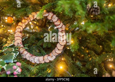 Londres, Royaume-Uni, Une couronne de Noël faite à la main à partir de tranches de pomme séchées est suspendue parmi des branches de sapin illuminées au marché de Spitalfields. Banque D'Images