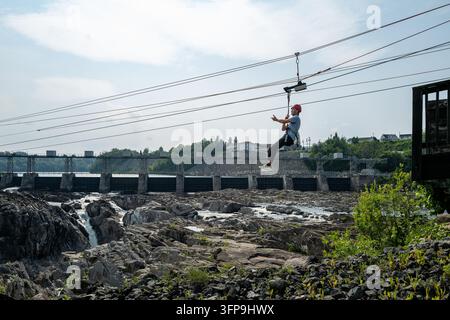 Une personne pratiquant le tyrolienne au-dessus d'une gorge rocheuse près d'un barrage, illustrant le tourisme d'aventure en plein air et les loisirs d'été. Banque D'Images