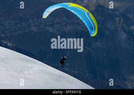 Vue d'un parapente planant au-dessus des pentes enneigées du Jungfraujoch avec des sommets montagneux rocheux en arrière-plan à Jungfraujoch, Valais, Suis Banque D'Images