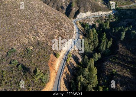 Une perspective aérienne par drone montre une route pavée en lacets serpentant le long de coteaux arides et de forêts de pins clairsemées. Monts Troodos Chypre Banque D'Images