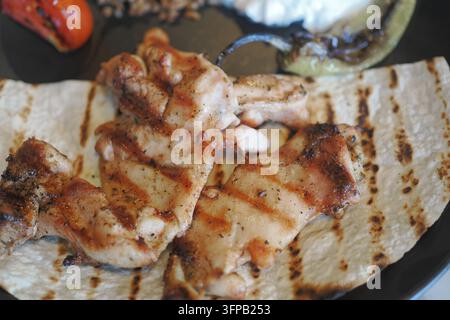 Pièces de poulet grillées sur une tortilla avec des légumes dans une assiette Banque D'Images
