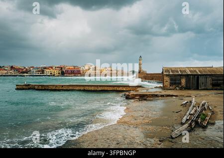 Des nuages d'orage s'accumulent au-dessus du port vénitien de Chania et de son phare historique alors que des mers agitées se brisent contre les murs du port, Crète, Grèce. Banque D'Images