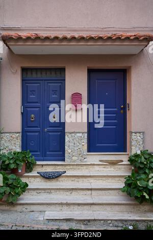 Deux portes bleues vibrantes avec une boîte aux lettres rouge sur un mur rose, comportant des marches en pierre et des plantes en pot, capturant l'architecture italienne Banque D'Images