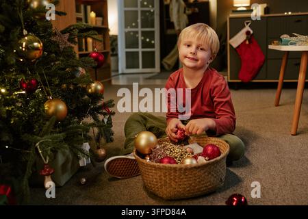 Portrait d'un garçon joyeux décorant le sapin de Noël à la maison Banque D'Images