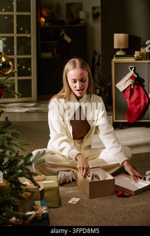 Femme ouvrant une boîte de cadeau de Noël près d'un arbre décoré à la maison Banque D'Images