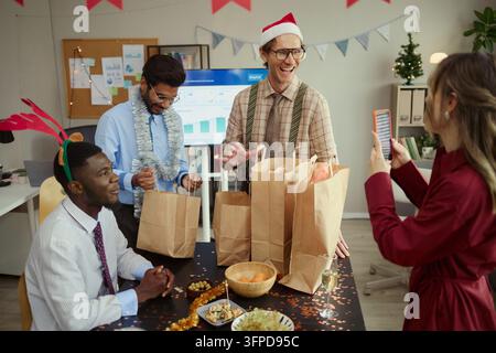 Femme prenant une photo de collègues divers déballant des cadeaux au bureau Banque D'Images