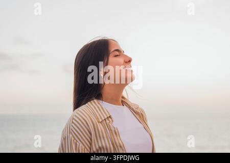 Jeune femme aux yeux fermés et avec un sourire doux, ressentant une liberté consciente et une paix intérieure en plein air, se sentant calme en prenant une profonde inspiration et en savourant Banque D'Images