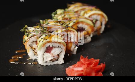 Rollettes de sushi gourmandes disposées sur une assiette en ardoise, garnies d'avocat, de saumon, de thon, de sauce et de graines de sésame Banque D'Images