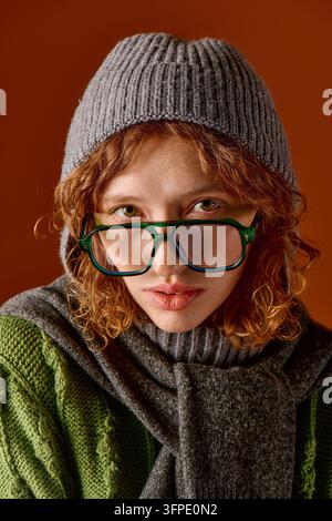 Une jeune femme aux cheveux bouclés porte un pull tricoté et un bonnet d'hiver, embrassant la saison froide. Banque D'Images