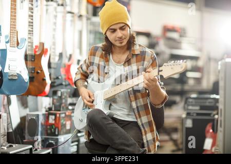 Jeune homme testant une guitare électrique dans un magasin de musique Banque D'Images