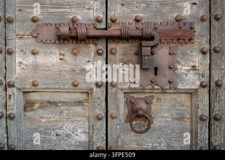 Close-up d'une porte en bois usée avec un lourd loquet rouillé, des rivets en fer et un heurtoir en forme d'anneau, Gubbio, Ombrie, Italie Banque D'Images