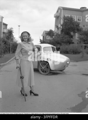 Luxe quotidien élégant en 1949 – une époque où la mode féminine était définie par des silhouettes moulantes, des tailles accentuées et une simplicité sophistiquée. La veste et la jupe assorties reflètent l'esthétique d'après-guerre – une tenue typique pour la femme suédoise moderne qui souhaitait être à la fois pratique et chic. Cette silhouette en sablier était inspirée du révolutionnaire « New Look » de Christian Dior, qui a fait sensation dans le monde de la mode en 1947. Derrière elle se trouve une microvoiture à trois roues, une construction personnalisée et artisanale utilisant des roues de moto à l'avant. Dans l'Europe d'après-guerre, les pénuries sévères de maté Banque D'Images